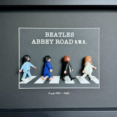 Tableau Abbey Road avec quatre figurines Playmobil traversant un passage piéton sur fond gris dans un cadre noir