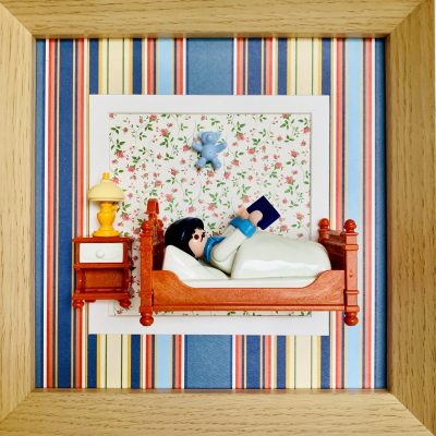 Tableau Alfred, figurine Playmobil lisant un livre au lit avec lampe jaune, table de chevet et ourson bleu