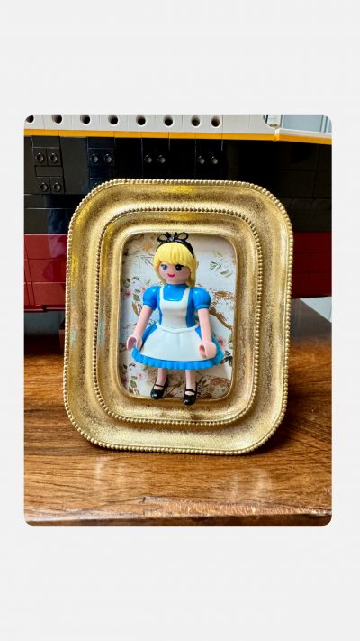 Tableau ALICE, figurine Playmobil en robe bleue et tablier blanc dans un cadre doré sur fond fleuri
