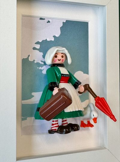 Figurine Bécassine en robe verte, coiffe blanche, valise et parapluie rouge, avec une oie, dans un cadre blanc