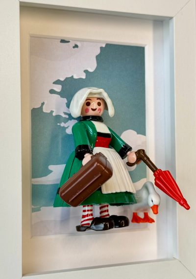 Figurine Bécassine en robe verte, coiffe blanche, valise, parapluie rouge et oie, dans un cadre blanc