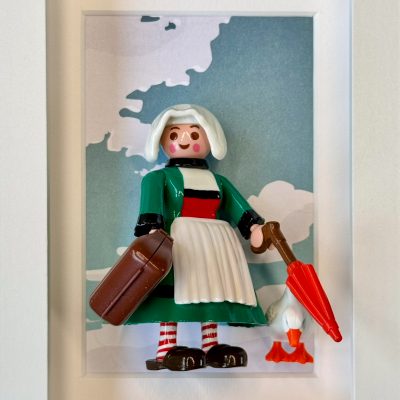 Figurine Bécassine en robe verte et tablier blanc, valise, parapluie rouge et oie, dans un cadre blanc
