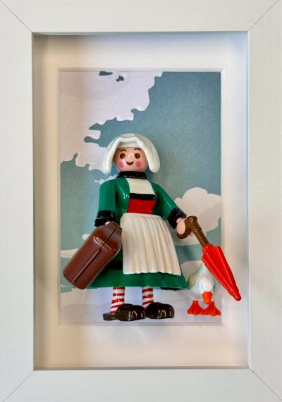 Figurine Bécassine en robe verte et tablier blanc, valise, parapluie rouge et oie, dans un cadre blanc