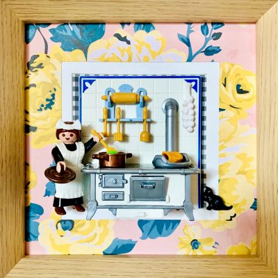 Tableau Désirée, figurine Playmobil de cuisinière en tablier blanc devant un fourneau ancien, chat noir et papier peint