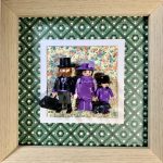 Tableau Family avec trois figurines Playmobil habillées de violet, chien noir, fond fleuri et cadre en bois clair