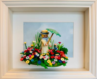 Tableau La Femme à l'ombrelle : figurine Playmobil en robe claire et chapeau, ombrelle verte, dans un massif de fleurs