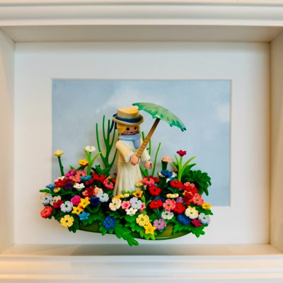 Tableau La Femme à l'ombrelle : figurine Playmobil en robe claire et chapeau, ombrelle verte, dans un massif de fleurs