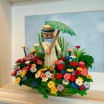 Figurine Playmobil en robe blanche tenant une ombrelle verte au milieu d'un champ de fleurs, tableau La Femme à l'ombrelle