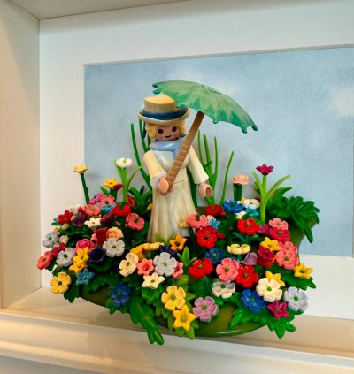 Figurine Playmobil en robe blanche tenant une ombrelle verte au milieu d'un champ de fleurs, tableau La Femme à l'ombrelle