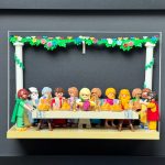 Tableau La Cène recréé en figurines Playmobil attablées sous une guirlande fleurie, dans un cadre noir 30x40 cm
