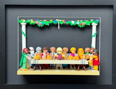 Tableau La Cène recréé en figurines Playmobil attablées sous une guirlande fleurie, dans un cadre noir 30x40 cm