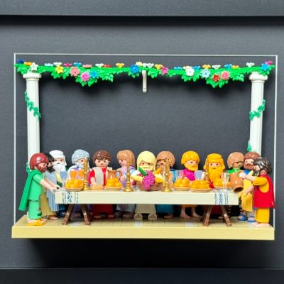 Tableau La Cène recréé en figurines Playmobil attablées sous une guirlande fleurie, dans un cadre noir 30x40 cm