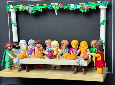 Scène de La Cène recréée en figurines Playmobil autour d'une longue table garnie de pains, fruits et carafe