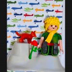 Detail du tableau Le Petit PRINCE : figurine blonde a echarpe jaune, renard rouge et rose sur fond d'avions