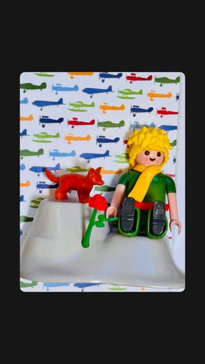Detail du tableau Le Petit PRINCE : figurine blonde a echarpe jaune, renard rouge et rose sur fond d'avions