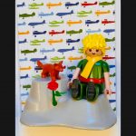 Tableau Le Petit PRINCE, figurine blonde à écharpe jaune assise sur une planète grise avec renard roux et rose rouge
