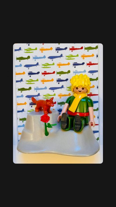 Tableau Le Petit PRINCE, figurine blonde à écharpe jaune assise sur une planète grise avec renard roux et rose rouge