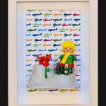 Tableau Le Petit PRINCE avec figurine blonde en tunique verte, renard roux et rose rouge sur fond d'avions colores