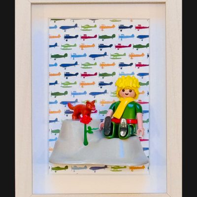 Tableau Le Petit PRINCE avec figurine blonde en tunique verte, renard roux et rose rouge sur fond d'avions colores