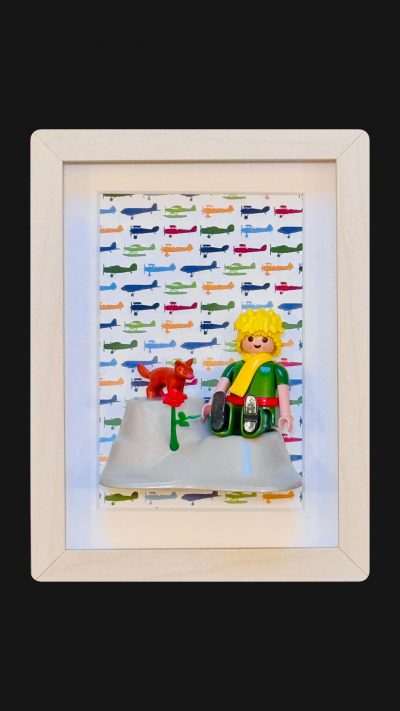 Tableau Le Petit PRINCE avec figurine blonde en tunique verte, renard roux et rose rouge sur fond d'avions colores