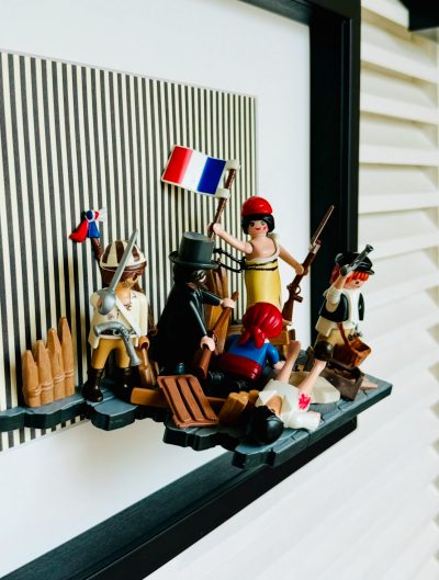 Détail de La Liberté guidant le peuple, figurines Playmobil en relief avec drapeau tricolore et fusils dans un cadre noir