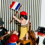 Figurine Playmobil en robe jaune brandissant un drapeau tricolore et un fusil, entouree d'insurges, oeuvre La Liberte