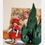 Figurine du Petit CHAPERON ROUGE avec panier et loup noir caché dans les sapins, sur fond de papier fleuri