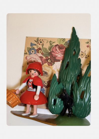 Figurine du Petit CHAPERON ROUGE avec panier et loup noir caché dans les sapins, sur fond de papier fleuri