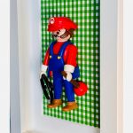 Figurine Super MARIO en salopette bleue avec ventouse et cle, encadree sur fond vichy vert dans un cadre blanc