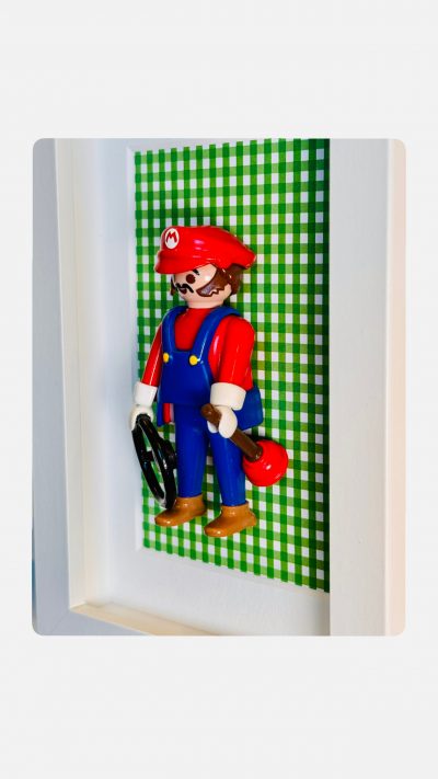 Figurine Super MARIO en salopette bleue avec ventouse et cle, encadree sur fond vichy vert dans un cadre blanc