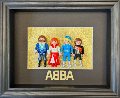 Tableau ABBA avec quatre figurines Playmobil costumées sur fond doré pailleté et lettrage ABBA, cadre bois gris