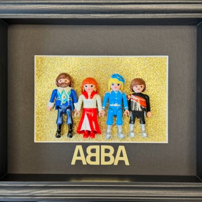 Tableau ABBA avec quatre figurines Playmobil costumées sur fond doré pailleté et lettrage ABBA, cadre bois gris