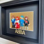 Tableau ABBA avec quatre figurines Playmobil en costumes disco sur fond doré pailleté, cadre noir profond