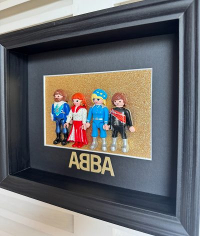 Tableau ABBA avec quatre figurines Playmobil en costumes disco sur fond doré pailleté, cadre noir profond