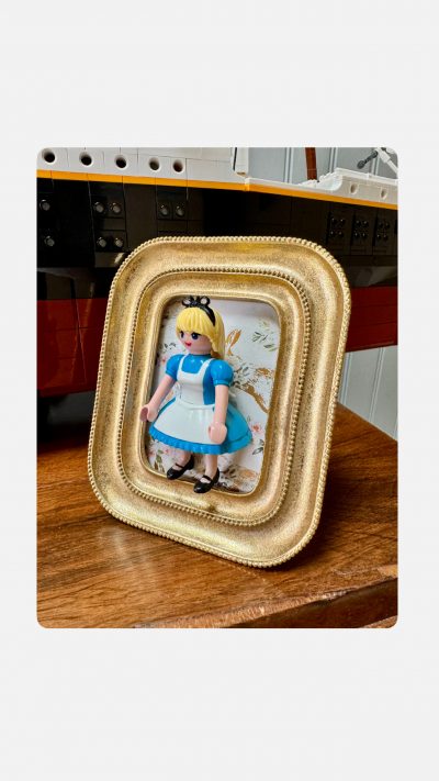 Tableau ALICE, figurine Playmobil en robe bleue et tablier blanc dans un cadre doré à perles sur fond fleuri