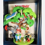 Tableau ASTÉRIX et OBÉLIX, figurines gauloises, chien blanc, sangliers et Romains suspendus dans un arbre, cadre noir