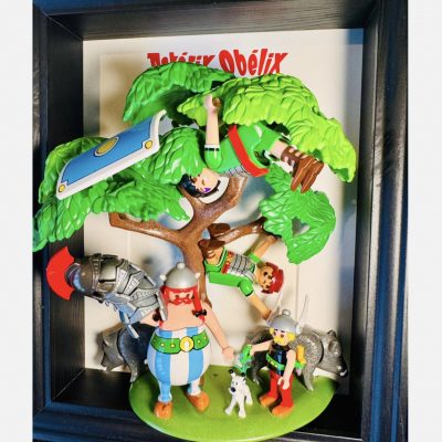 Tableau ASTÉRIX et OBÉLIX, figurines gauloises, chien blanc, sangliers et Romains suspendus dans un arbre, cadre noir