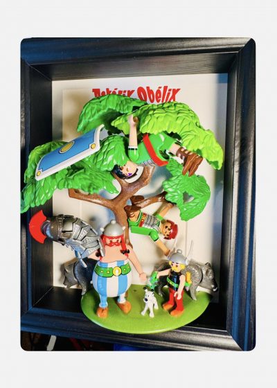 Tableau ASTÉRIX et OBÉLIX, figurines gauloises, chien blanc, sangliers et Romains suspendus dans un arbre, cadre noir