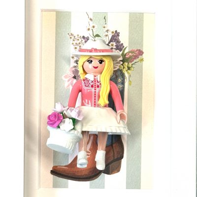 Tableau Cowgirl : figurine Playmobil blonde en robe rose, chapeau fleuri et panier de roses, devant une botte de cowboy