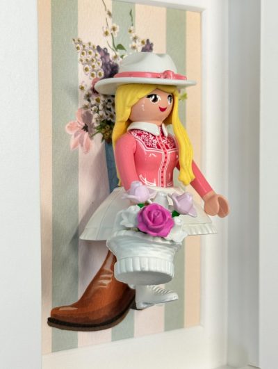 Figurine Playmobil blonde au chapeau blanc et corsage rose tenant un panier de roses, tableau Cowgirl