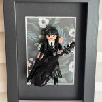 Tableau MERCREDI, figurine Playmobil en robe noire jouant du violoncelle sur fond floral, dans un cadre noir