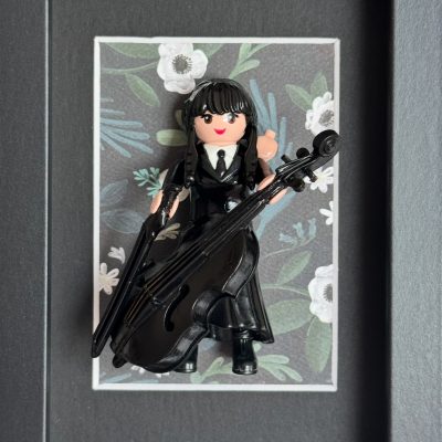 Tableau MERCREDI, figurine Playmobil en robe noire jouant du violoncelle sur fond fleuri, cadre noir 10x15 cm