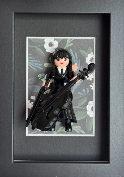Tableau MERCREDI, figurine Playmobil en robe noire jouant du violoncelle sur fond fleuri, cadre noir 10x15 cm