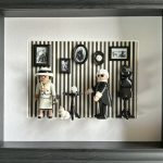 Tableau Rue Cambon avec deux figurines Playmobil, couturière en tailleur clair et créateur en noir, sur mur rayé