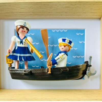 Tableau Toi, moi et l'Atlantique avec deux figurines Playmobil en tenue de marin dans une barque noire, cadre en bois clair