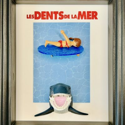 Tableau en figurines playmobil représentant l'affiche du film les dents de la mer avec une femme qui se baigne et en dessous un requin qui s'approche d'elle dangereusement