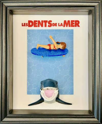 Tableau en figurines playmobil représentant l'affiche du film les dents de la mer avec une femme qui se baigne et en dessous un requin qui s'approche d'elle dangereusement