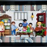 Six figurines Playmobil représentant les 6 acteurs phares de la série Friends sont disposés dans un cadre noir représentant une scène du café avec un buffet, une table basse avec gâteaux, une lampe murale, un fauteuil vert et un tableau sur un mur briqué.