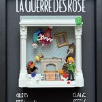 Scène miniature dans un cadre noir avec le titre "La Guerre Des Rose" en haut, montrant deux figurines : un homme renversé suspendu à un lustre rose et une femme blonde en vert tenant une hache, avec des meubles renversés, un tapis, un portrait incliné et une horloge ancienne.