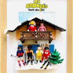 Six figurines miniatures représentant des personnages en tenue de ski colorée (rouge, rose, bleu, noir, jaune), posées devant un chalet en bois avec balcon, décor de neige et sapin vert, dans un cadre en bois naturel avec le titre jaune et noir "Les Bronzés font du ski" en haut.